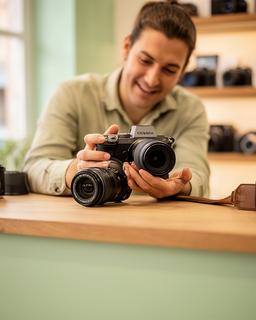 Especialista revisando una cámara mirrorless y un objetivo en el mostrador de una tienda de fotografía